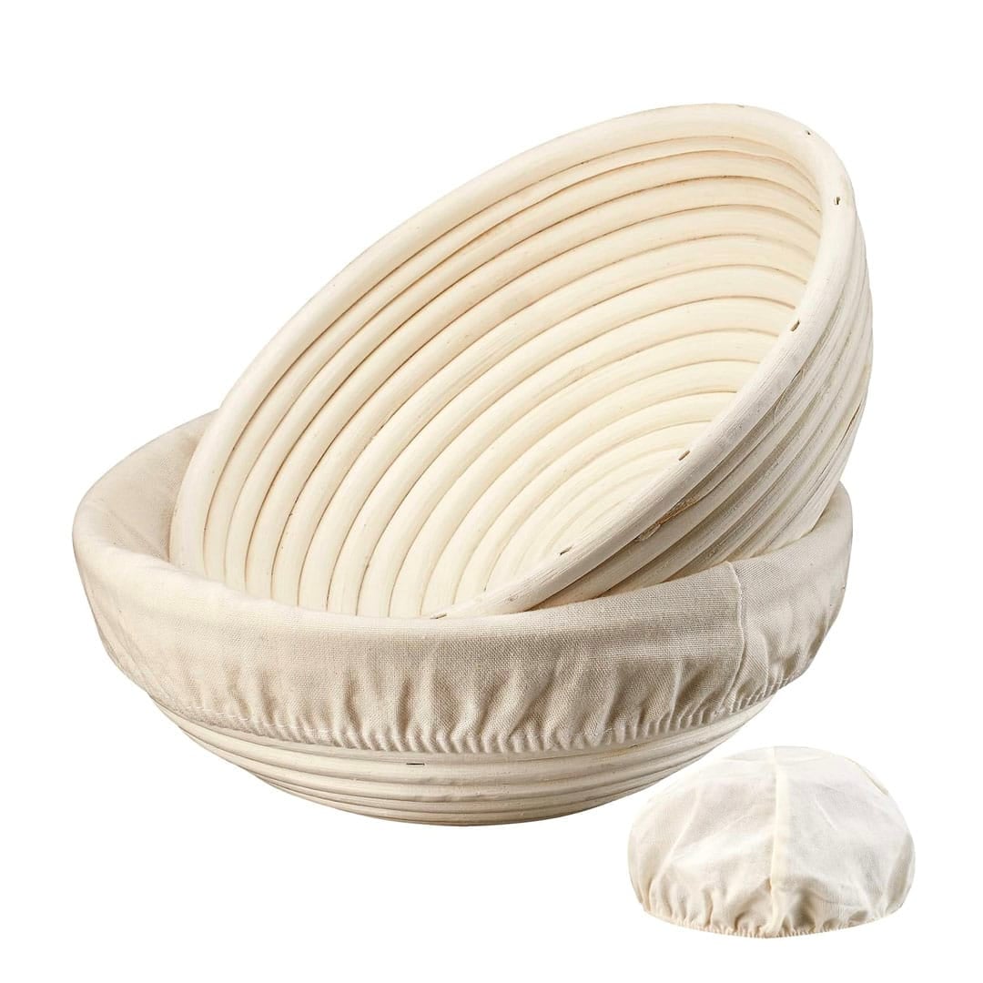 Two round, light-colored bread proofing baskets with spiral grooves, one inside the other, and a separate cloth liner displayed in front—the perfect set for anyone following the ultimate homemade bread guide.