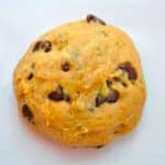 A round ball of dough with visible chocolate chips and green specks sits on a white surface, ready to be baked.