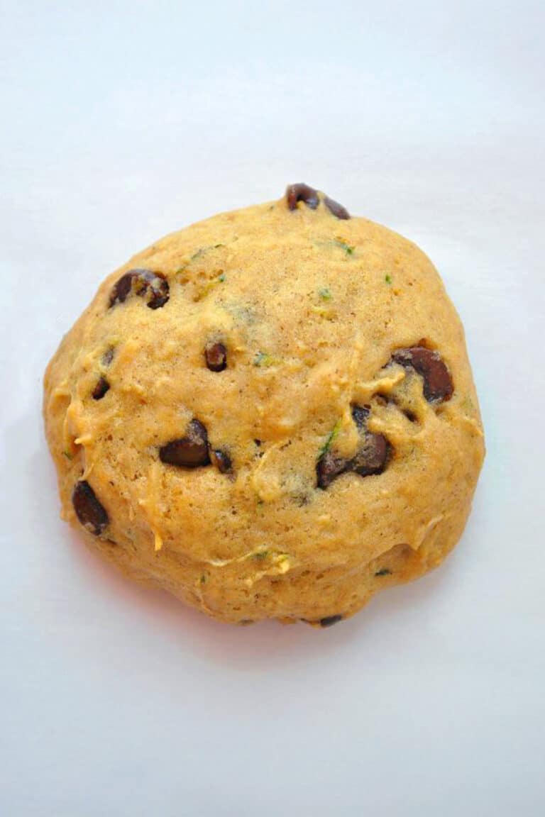 A round ball of dough with visible chocolate chips and green specks sits on a white surface, ready to be baked.