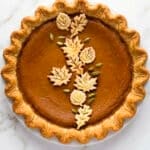 A round pumpkin pie with a crimped crust, decorated with pastry leaves and seeds in a vine pattern, perfect for the best pumpkin recipes.