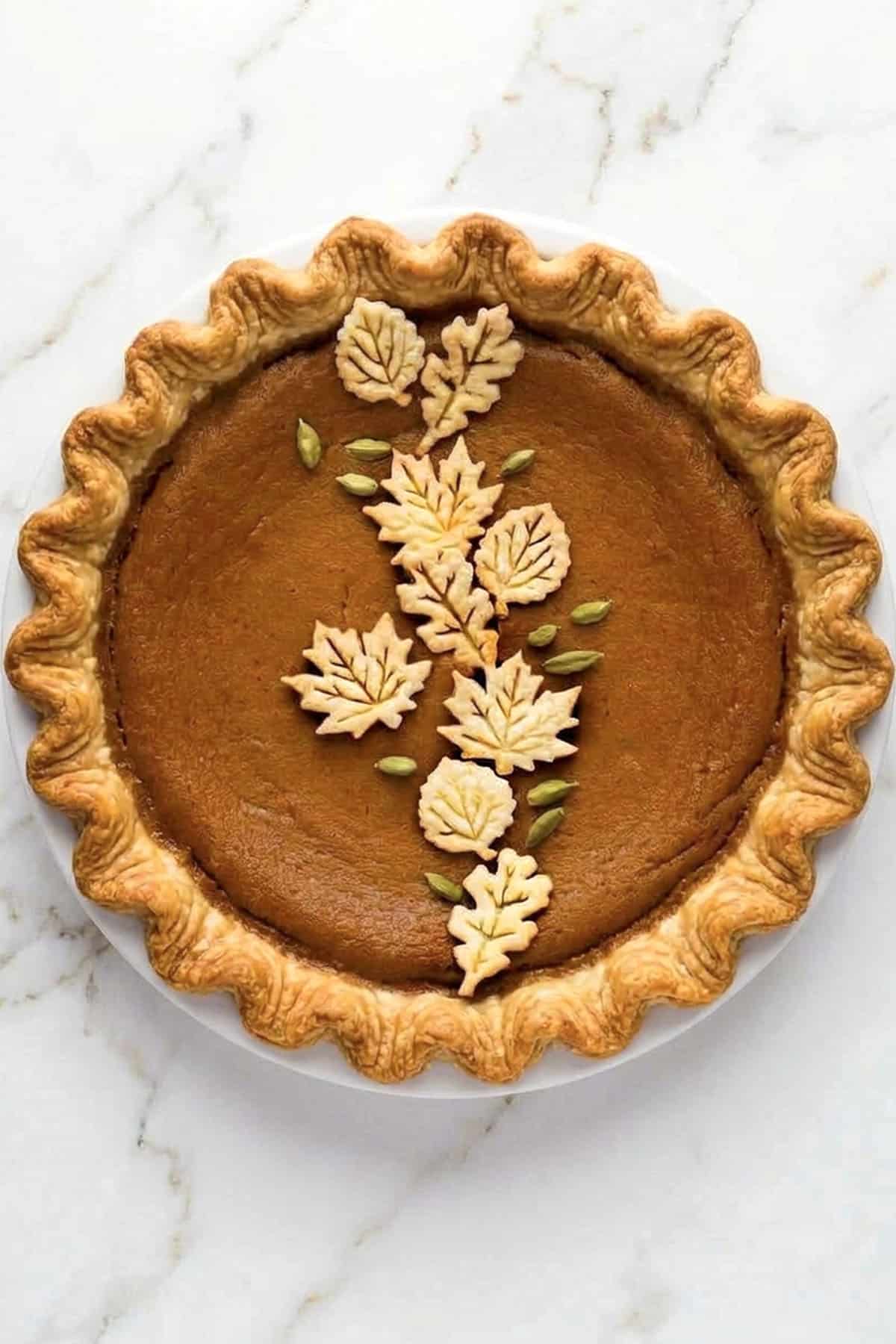 A round pumpkin pie with a crimped crust, decorated with pastry leaves and seeds in a vine pattern, perfect for the best pumpkin recipes.