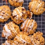 Pumpkin oatmeal chocolate chip cookies drizzled with white icing on a wire cooling rack with cinnamon sticks.