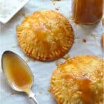 Two hand pies drizzled with caramel sauce, with a small jar of caramel, a spoon, and a dish of coarse salt nearby.