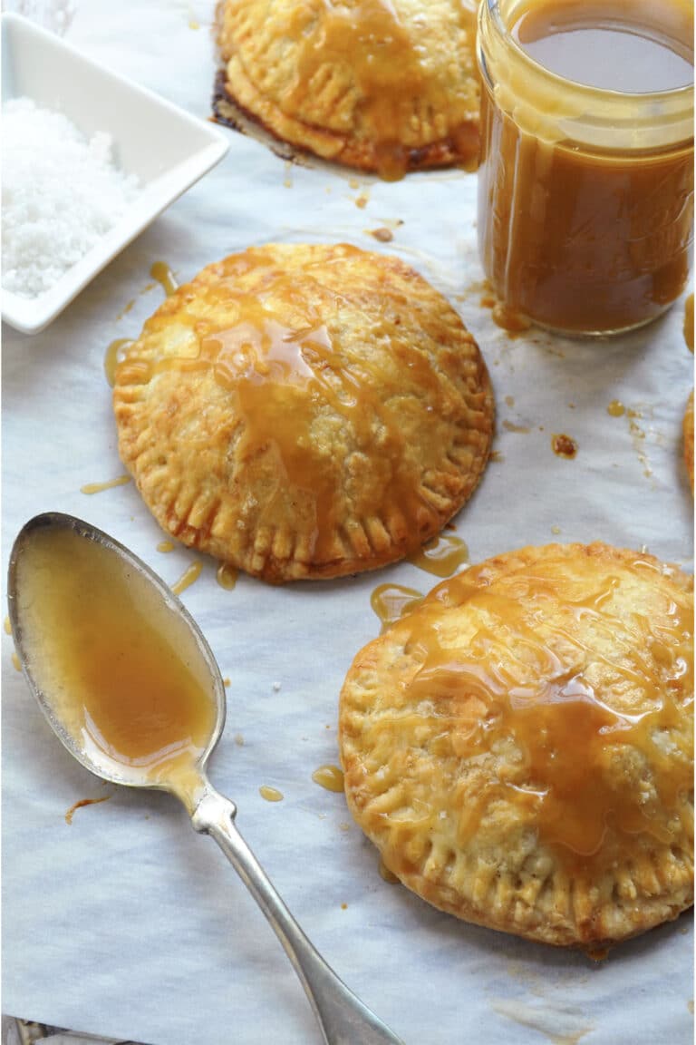 Two hand pies drizzled with caramel sauce, with a small jar of caramel, a spoon, and a dish of coarse salt nearby.